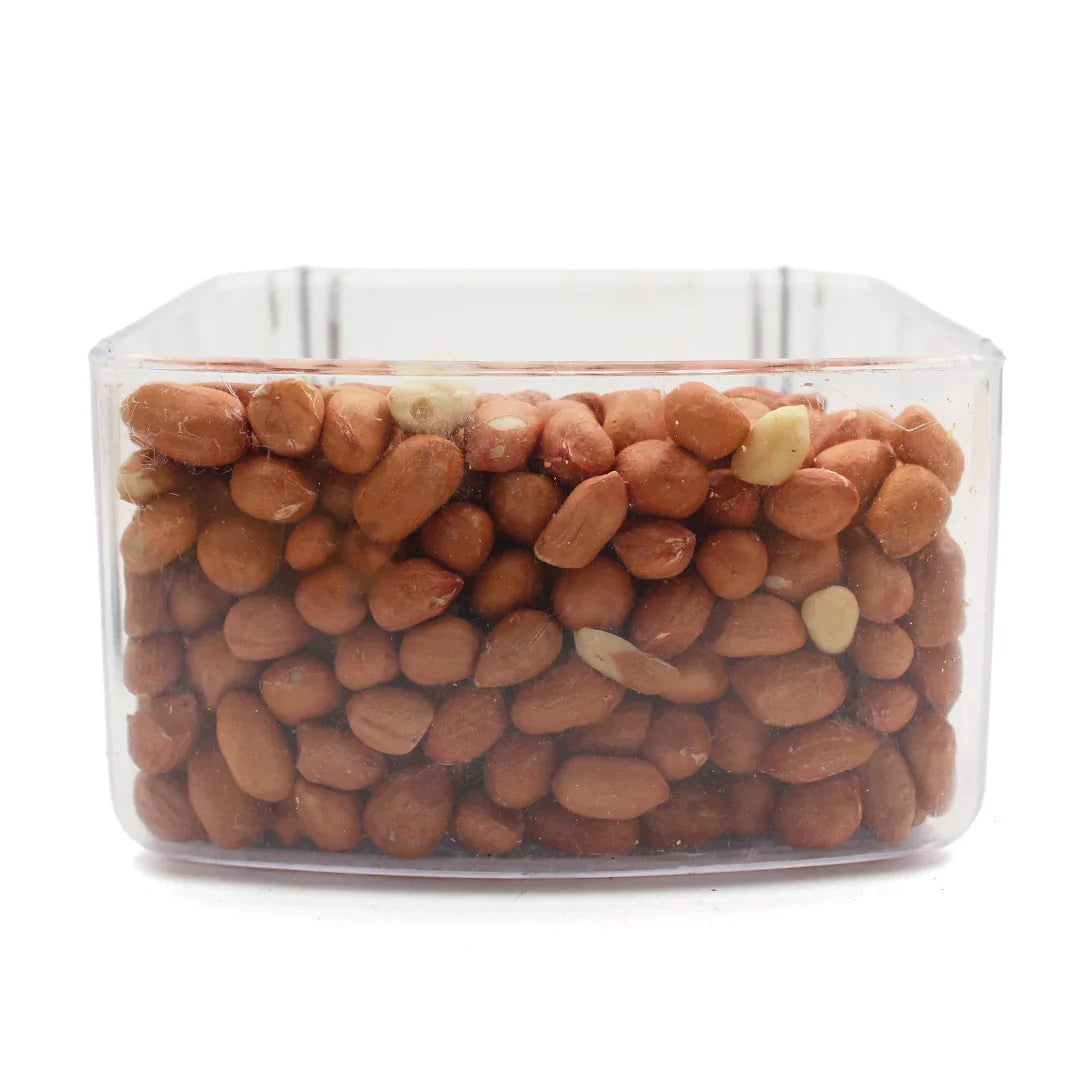 Clear plastic container filled with whole raw peanuts with skin against white background