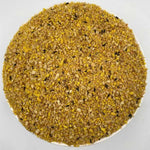 Close-up of yellow granular mix with small black seeds on a white surface