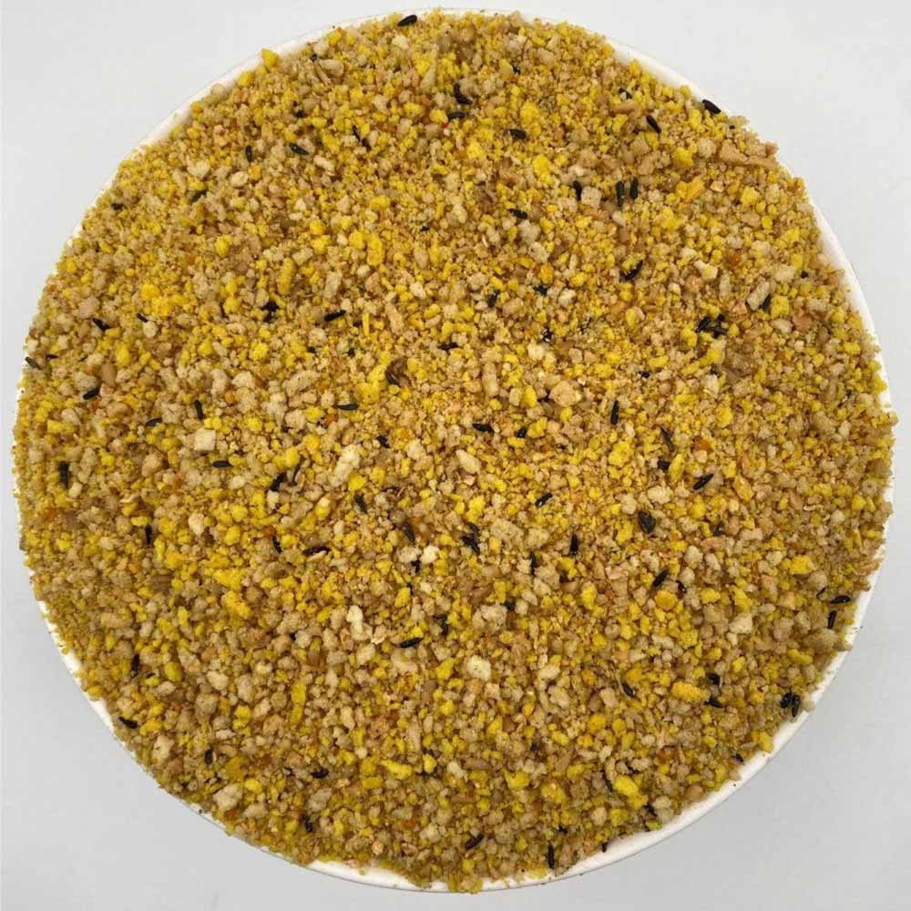 Close-up of yellow granular mix with small black seeds on a white surface